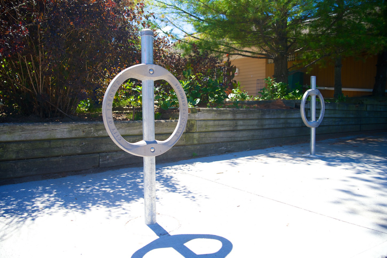 Commercial outdoor bike rack high capacity with bicycle secured on a concrete pad in a park setting for public spaces, schools, and businesses.